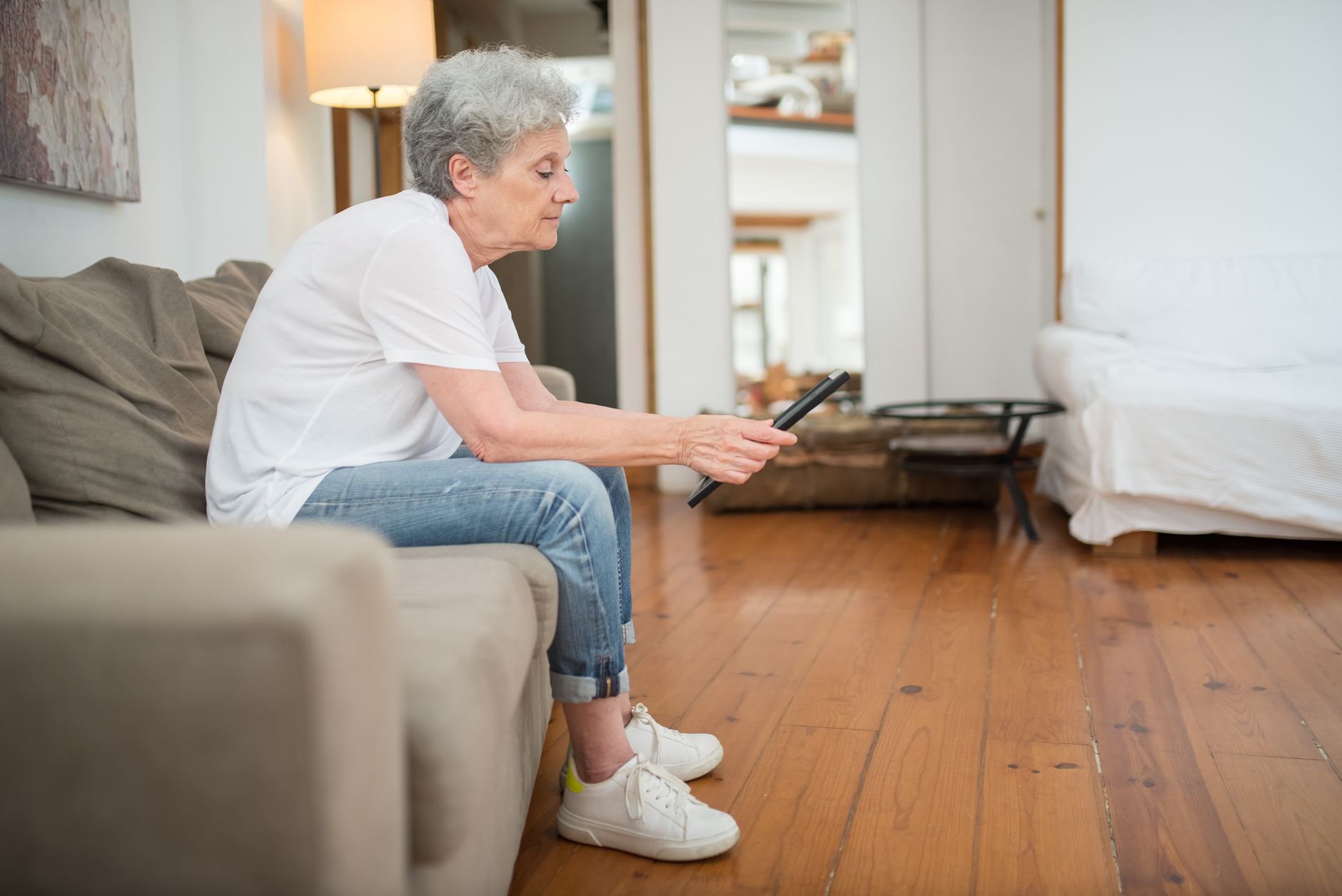 Older woman sitting on a couch holding a tablet in a cosy living room