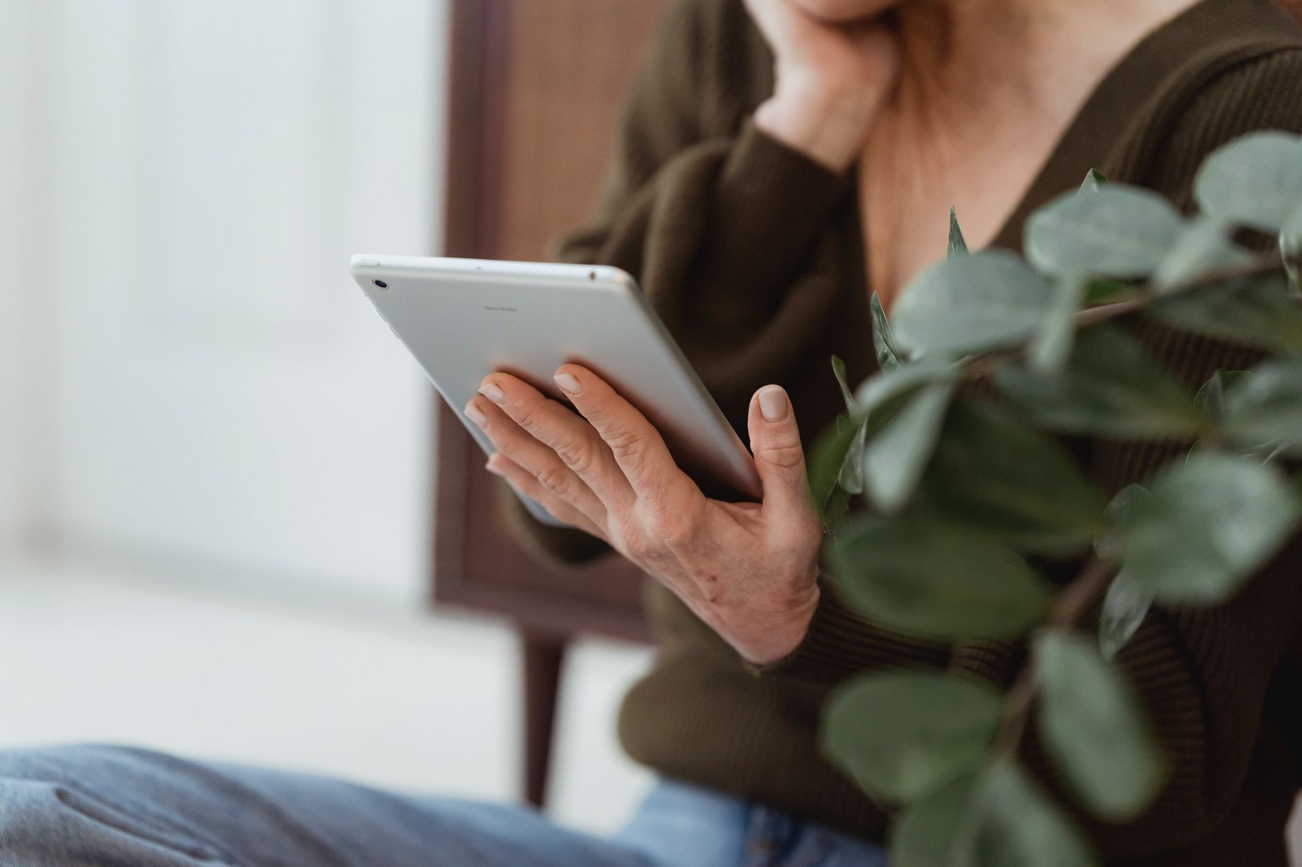 Close crop of a woman at home checking her phone screen, with a plant blurred in the background